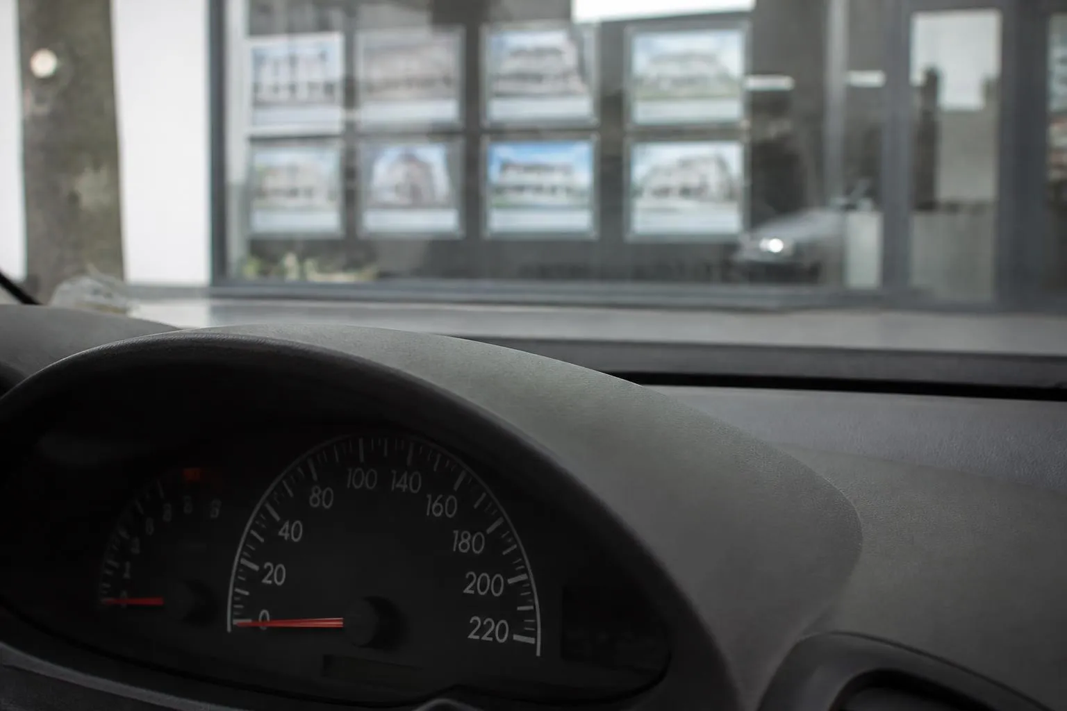 Compteur kilométrique d'une voiture garée devant la vitrine d'une agence immobilière